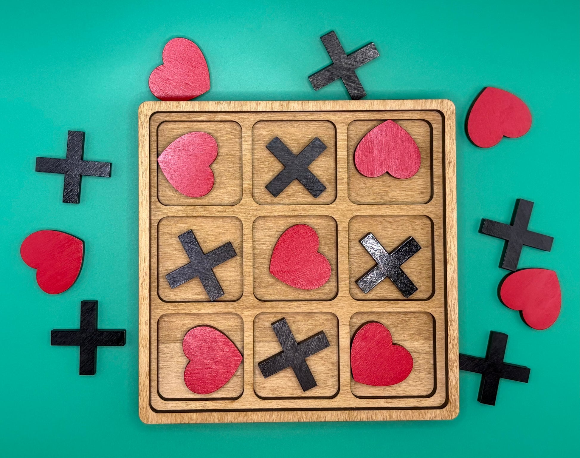 Wooden tic-tac-toe board with heart-shaped game pieces on a teal background