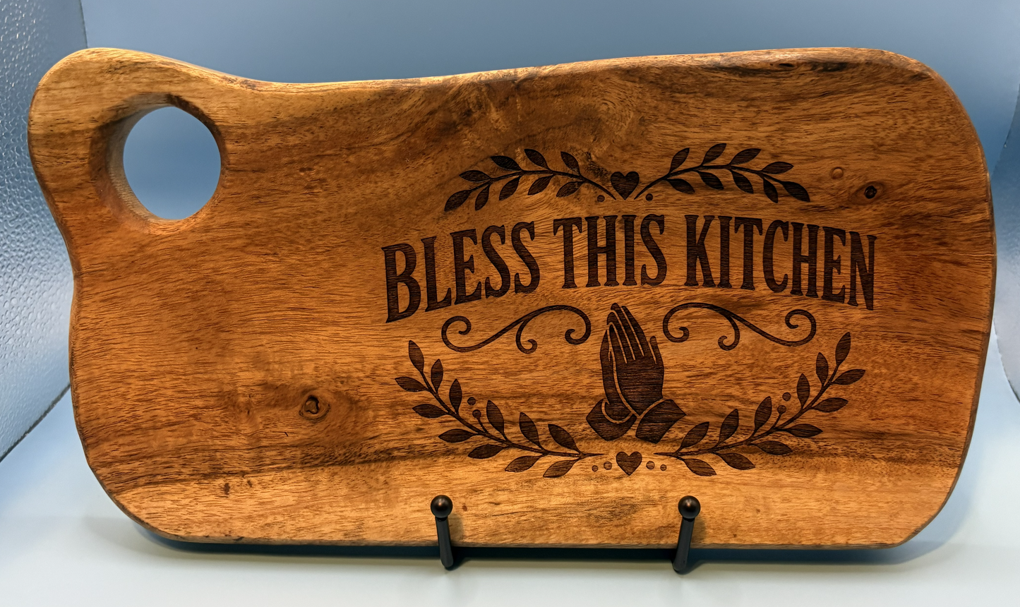 Wooden cutting board with 'Bless This Kitchen' engraving on a light blue background