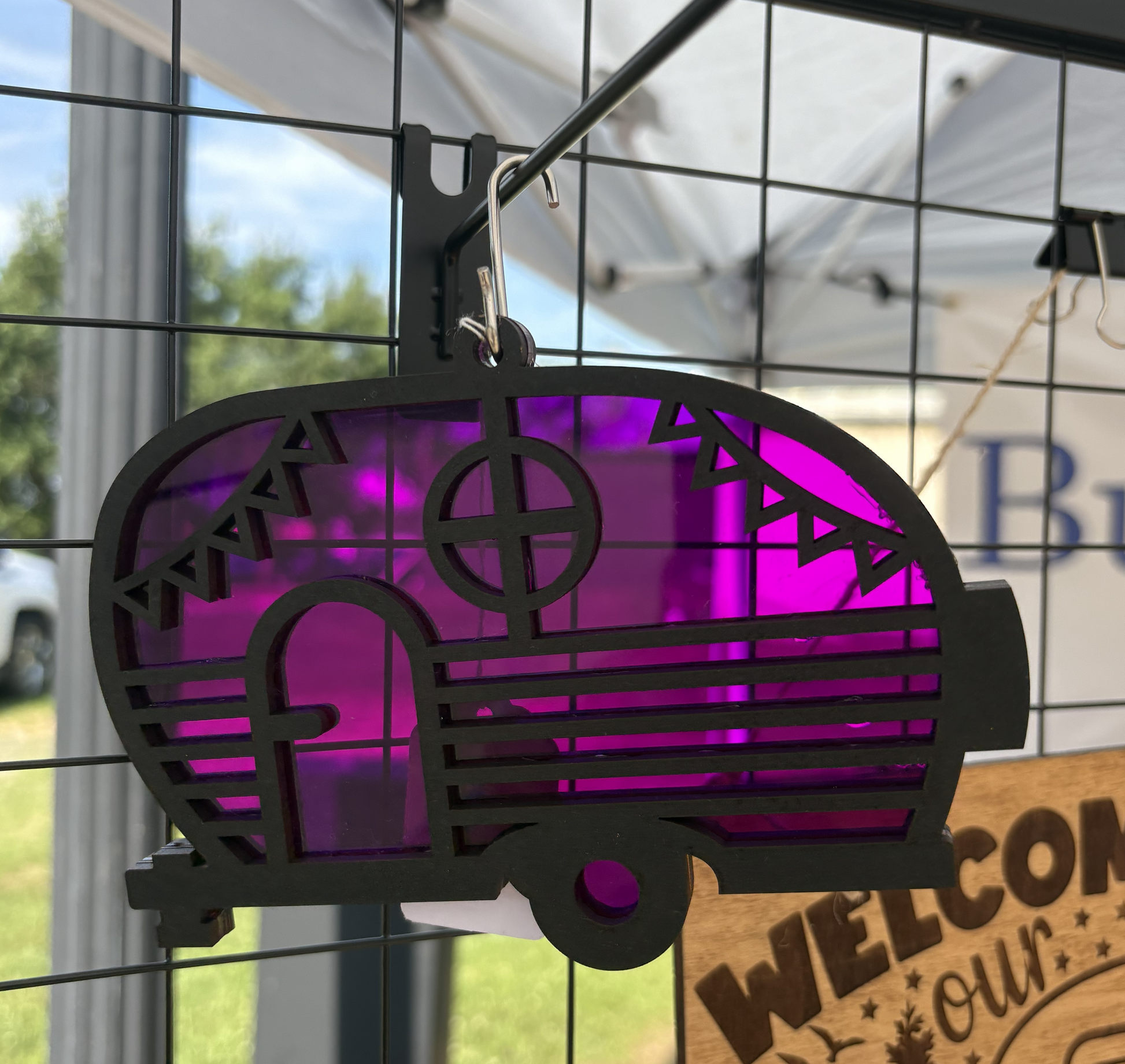 Decorative metal sign with purple interior and cut-out design, hanging against a window.