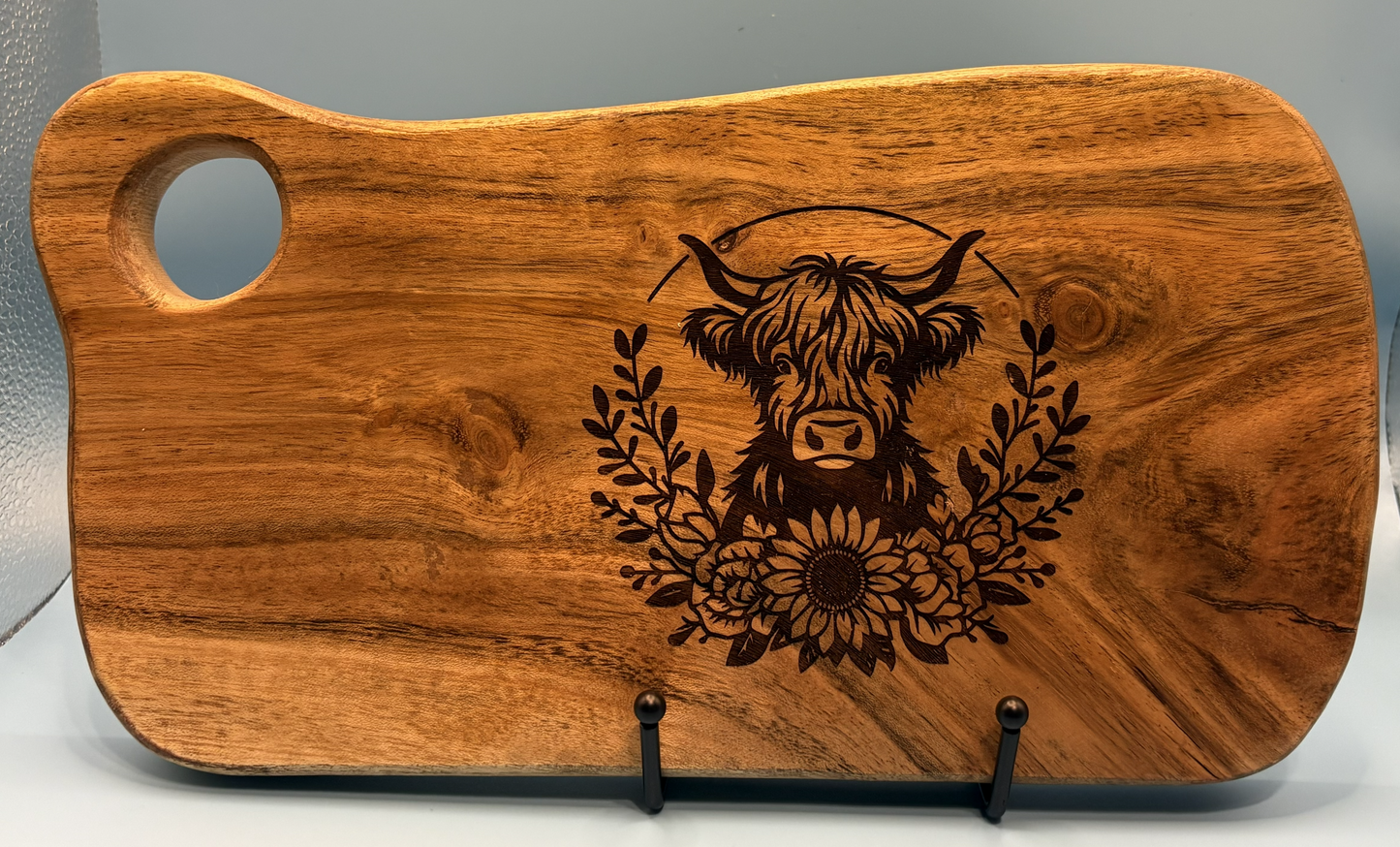 Wooden cutting board with engraved highland cow design on a gray background