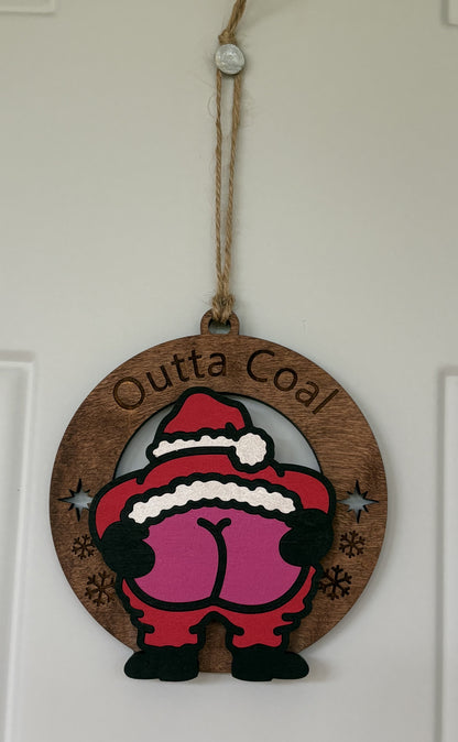 A round wooden Christmas door hanging ornament with a cartoon poop character wearing a Santa hat and the words 'Outta Coal' engraved on a white door.